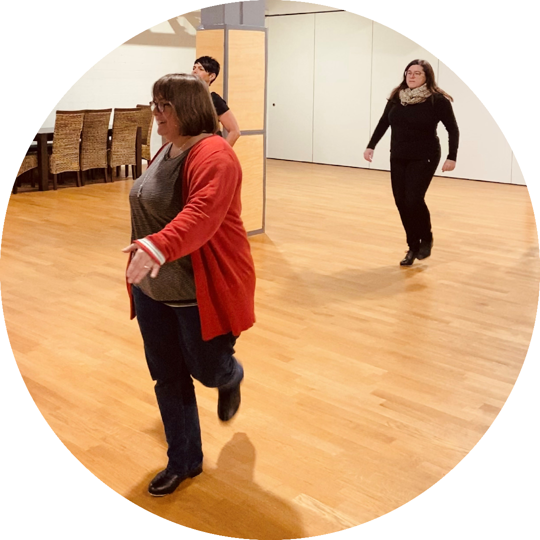 Stepptanzlehrerin im Kurs mit Teilnehmern im Hintergrund